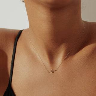 Gold necklace with a pendant on a person wearing a black top against a neutral background