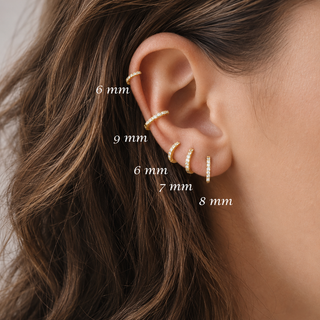 Close-up of a person's ear wearing multiple gold ear cuffs in different sizes, with white text labels showing millimeter measurements: 6 mm, 9 mm, 6 mm, 7 mm, and 8 mm.