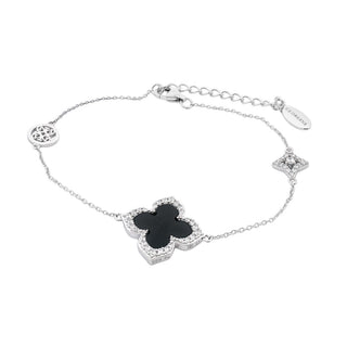 A delicate silver chain bracelet featuring a central black four-leaf clover charm with a silver border, accompanied by a small silver monogram charm and a round silver medallion, displayed on a clean white background.