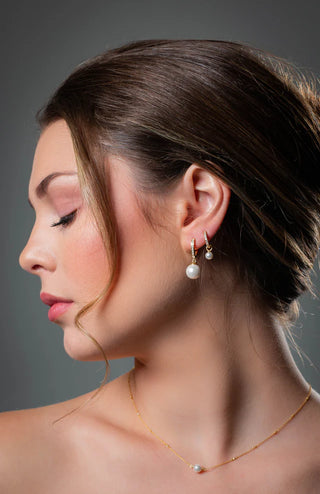 Close-up of a woman wearing pearl earrings and a necklace against a gray background