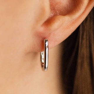 Silver hoop earring worn on a person's ear with a blurred background