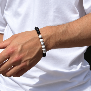 A close-up of a person's wrist wearing a beaded bracelet made of alternating black and white beads, worn with a white t-shirt.