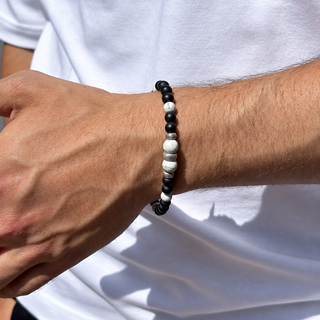 A close-up of a person's wrist wearing a beaded bracelet with alternating black and white beads, worn over a white t-shirt.