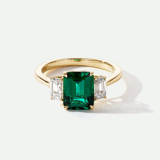 Gold ring with a green gemstone and two diamonds on a white background