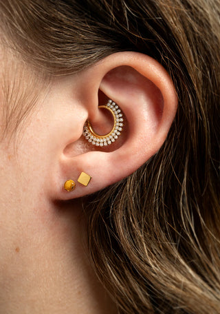 Close-up of an ear wearing gold hoop earrings with small stones and gold studs.