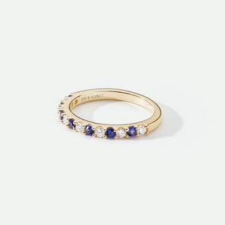 Gold ring with blue and white gemstones on a light gray background
