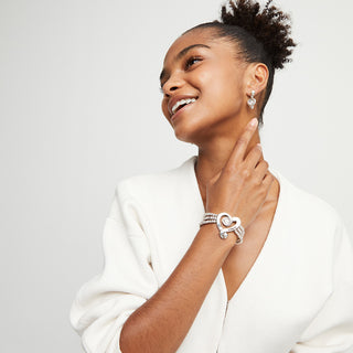 Woman wearing a silver bracelet and earrings on a plain background