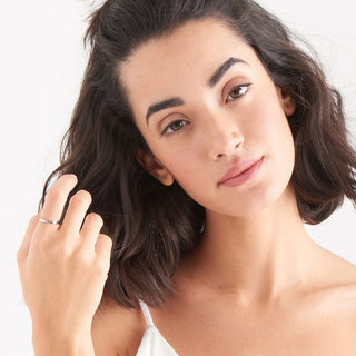 Woman with short brown hair touching her hair against a white background