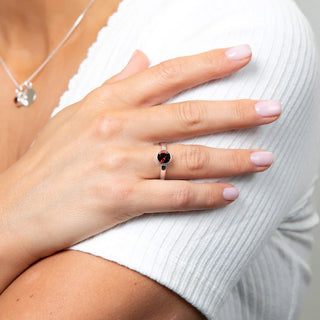 Close-up of a hand wearing a silver ring with a red gemstone on a white background