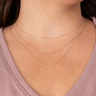 Close-up of a person wearing three thin gold necklaces on a plain background