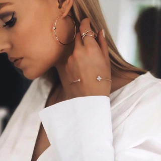 Close-up of a woman wearing gold hoop earrings, a ring, and a bracelet with a blurred background.