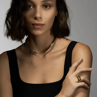 Woman wearing a black top and gold necklace with a neutral background