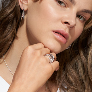 Close-up of a woman wearing silver hoop earrings and a ring, with a soft focus on her face.
