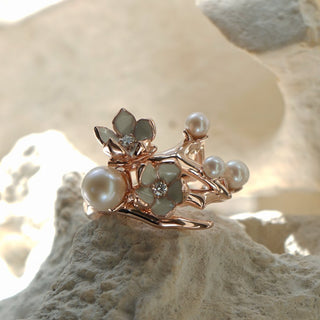 Rose gold ring with pearls and gemstones on a textured beige surface