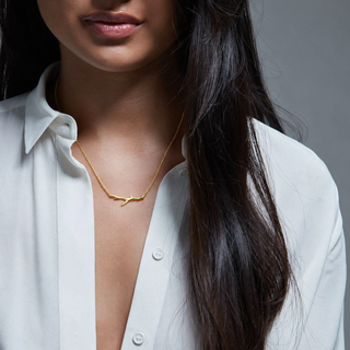 Woman wearing a diamond branch shaped gold necklace against a gray background