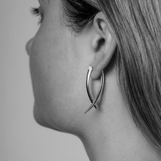 Close-up of a woman wearing a silver hoop earring on a plain background