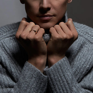 Person wearing a gray sweater with hands clasped in front, against a dark background