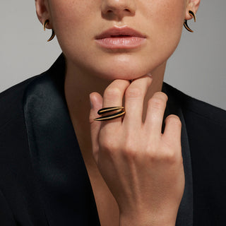 Close-up of a person wearing a gold ring with black stripes, black blazer, and earrings.