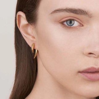 Close-up of a woman wearing gold hoop earrings with a neutral background
