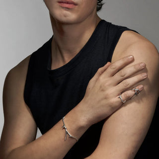 Person wearing silver jewelry on arms against a neutral background