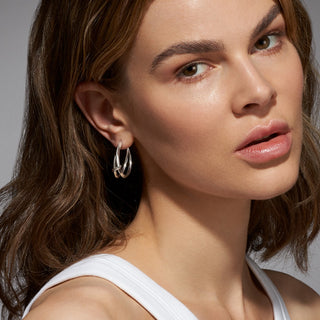Close-up of a woman wearing silver hoop earrings with a neutral background