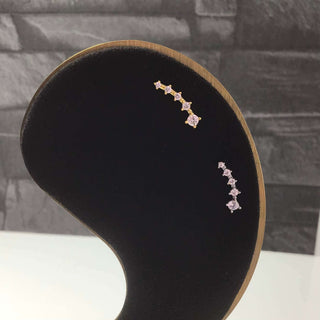 A pair of silver cartilage climber earrings with five graduated cubic zirconias, displayed on a black stand.