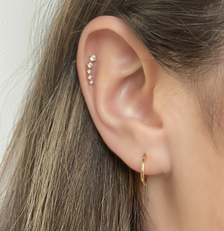 Close-up of an ear with gold earrings against a neutral background