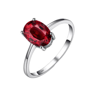A silver ring featuring an oval-cut, deep red gemstone in a four-prong setting, shown on a light gray background.