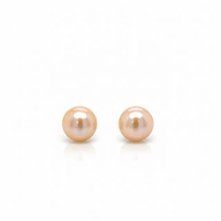 A pair of round freshwater pearl stud earrings in a soft peach-pink hue, displayed on a clean white background with subtle reflections below.