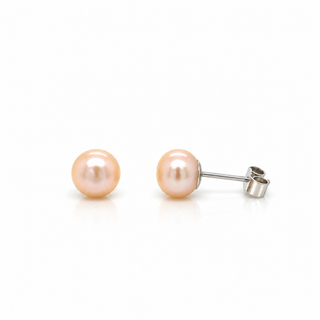 A pair of peach-colored freshwater pearl stud earrings with silver posts, shown on a clean white background with one earring facing forward and the other showing the side profile.