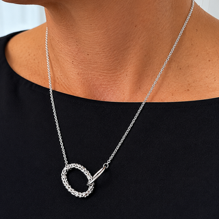 Silver necklace with a circular pendant worn by a person against a neutral background