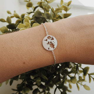 Silver bracelet with a circular cutout design on a wrist against a green leafy background