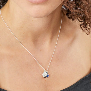 Necklace with a heart-shaped pendant featuring a blue gemstone on a person's neck.