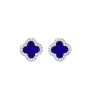 A pair of clover-shaped stud earrings with deep blue enamel centers and silver-toned borders set with small clear stones, shown on a light gray gradient background.
