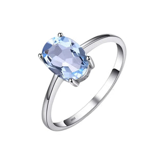 A silver ring featuring an oval-cut light blue gemstone in a four-prong setting, shown on a light gray background.