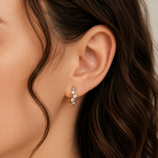 A close-up of a model's ear wearing a small silver huggie hoop earring adorned with clear cubic zirconia stones.