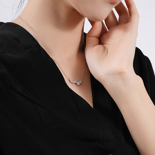 Person wearing a delicate necklace with a close-up of the jewelry on a plain background