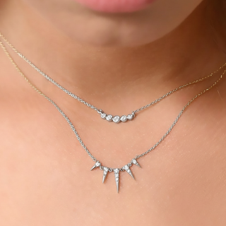 Two necklaces with spike designs on a person's neck against a neutral background