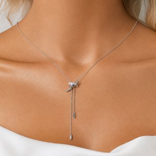 A silver Y-necklace with a bow-shaped charm set with clear crystals and two dangling chain ends, shown worn on a model's neck and upper chest.
