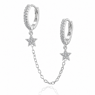 A pair of silver huggie hoop earrings adorned with clear pavé stones and dangling star charms connected by a delicate chain, shown on a white background with a faint reflection.