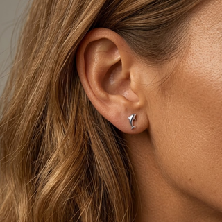 Close-up of an ear wearing a small dolphin shape earring with a neutral background