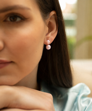 Close-up of a woman wearing pink pearl earrings with a blurred background