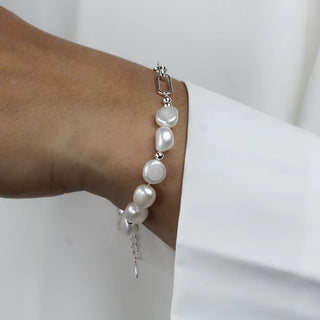 A close-up of a silver-toned bracelet with irregular white baroque pearls, worn on a person's wrist against a white shirt cuff.