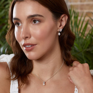 Woman wearing pearl earrings and necklace with a blurred green and brown background