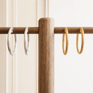 Two pairs of hoop earrings, one silver and one gold, hanging on a wooden rod against a neutral background.