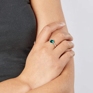 Hand wearing a ring with a green gemstone on a plain background