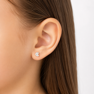 A close-up of a person's ear wearing a small silver stud earring with a clear flower-shaped crystal. The background is a clean white studio backdrop.