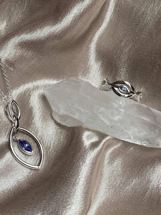 Silver eye-shaped pendant with a blue gemstone on a beige fabric background