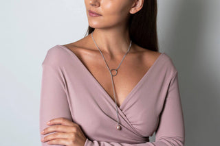 Woman wearing a pink dress with a necklace against a plain background