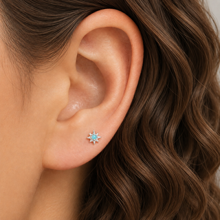 A close-up of a person's ear wearing a small silver-toned starburst stud earring with a light blue center stone.
